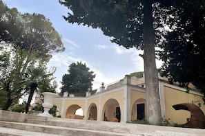 Un bâtiment doté de plusieurs arcades, d’un balcon et d’un grand arbre.