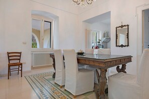 A dining area with a marble table, white upholstered chairs, a chandelier, and a view through an arched window. - Villa 'Luciana' with Private Terrace, Wi-Fi, and Air Conditioning (Martina Franca)