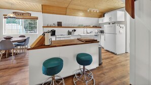 Moderni keittiö, jossa on puupalkkeja, valkoiset kaapit, suuri keittiösaareke, baarituolit ja kyltti, jossa lukee ”Happy Hour”.