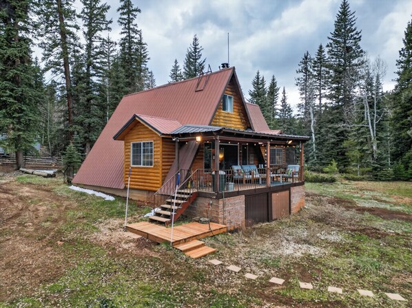 Eine Blockhütte mit Veranda und Gartenmöbeln, umgeben von Bäumen.