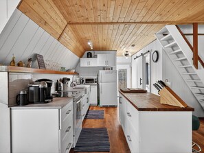 Eine kleine Küche mit weißen Schränken, einer Holz Arbeitsplatte, einem eingebauten Herd und einer Mikrowelle.