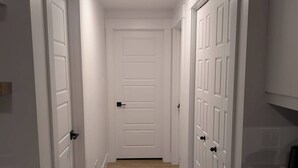 A narrow hallway with white doors and a wooden floor. - Charming Haven House (Moncton)