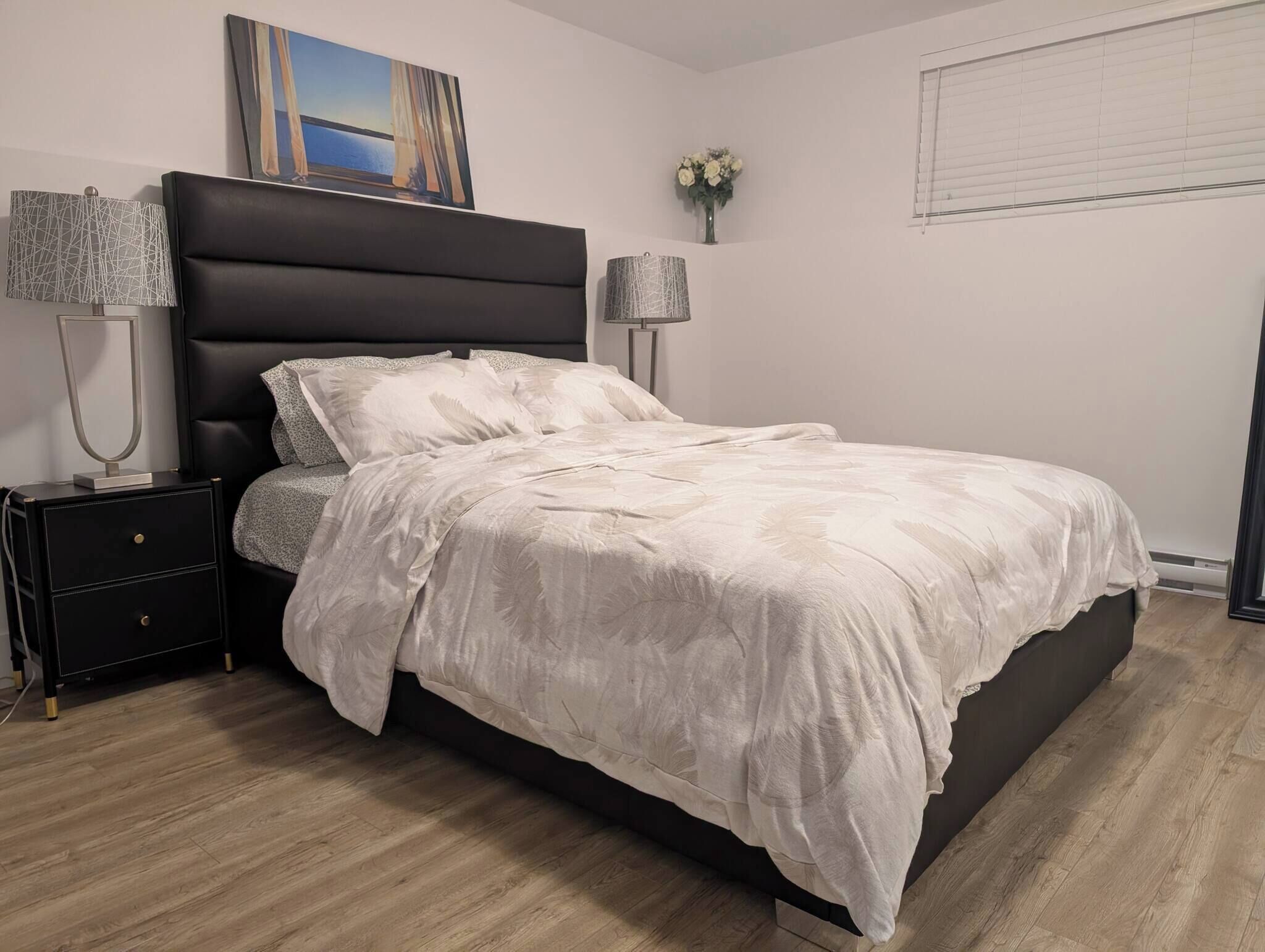 Une chambre à coucher avec un lit, des tables de chevet, une lampe, un tableau et une fenêtre.