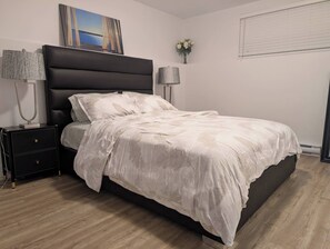 A bedroom with a bed, nightstands, a lamp, a painting, and a window.