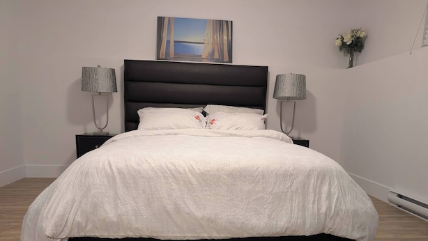 A bed with a white bedspread, a dark headboard, and two bedside lamps. - Charming Haven House (Moncton)