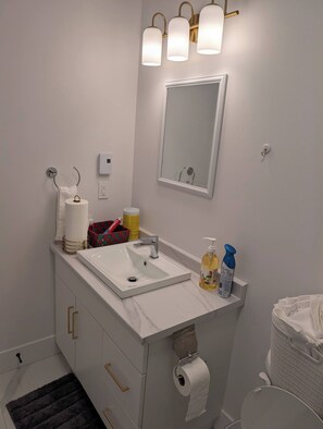 A bathroom with a white sink, a mirror, a towel rack, a toilet, and a trash bin.