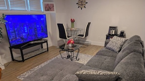 A living room with a sofa, a coffee table, a TV, and a dining area with chairs and a vase of flowers. - Charming Haven House (Moncton)