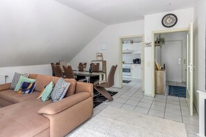 A modern living room with a sofa, dining table, chairs, and a kitchen in the background. - Cozy Apartment in Willingen, Usseln – Lovingly Furnished for a Relaxing Atmosphere (Willingen (Upland))
