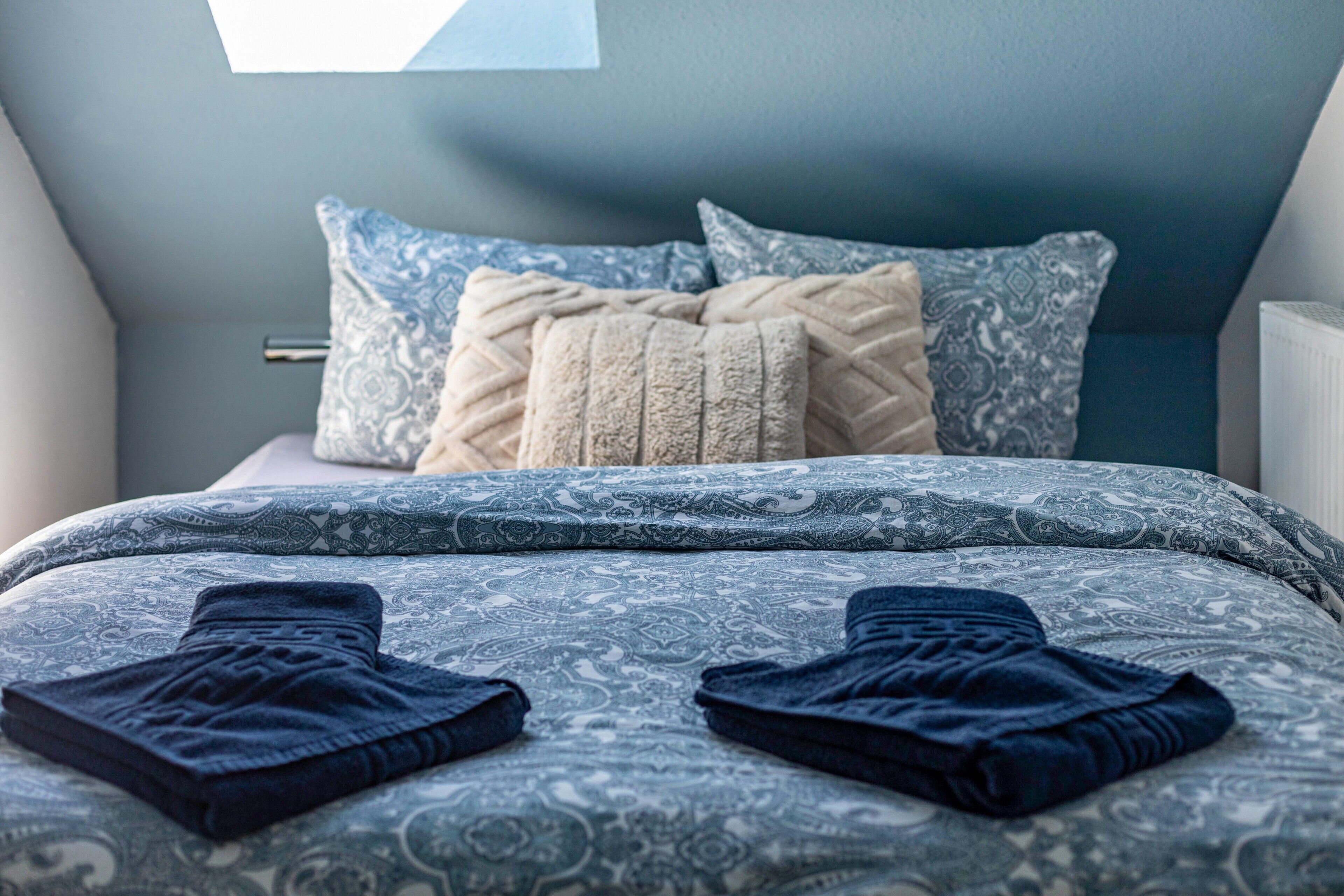 Ein Schlafzimmer mit einem gemusterten Bettüberwurf, zwei Kissen und einer gefalteten Decke auf dem Bett.