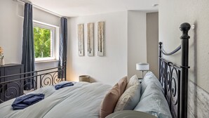 A bedroom with a bed, curtains, a lamp, and wall art. - Cozy Apartment in Willingen, Usseln – Lovingly Furnished for a Relaxing Atmosphere (Willingen (Upland))