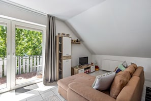 Een gezellige woonkamer met een bank, televisie en een balkon met uitzicht op bomen.