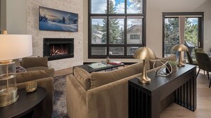 Ein Wohnzimmer mit Kamin, großen Fenstern, einem Sofa, einem Couchtisch und einer Lampe.