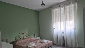 Quarto com cama, mesa de cabeceira, abajur e janela com cortinas.