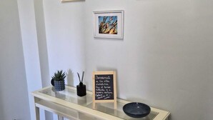 Paredes brancas com três quadros, uma mesa pequena com um letreiro de lousa e uma tigela preta.
