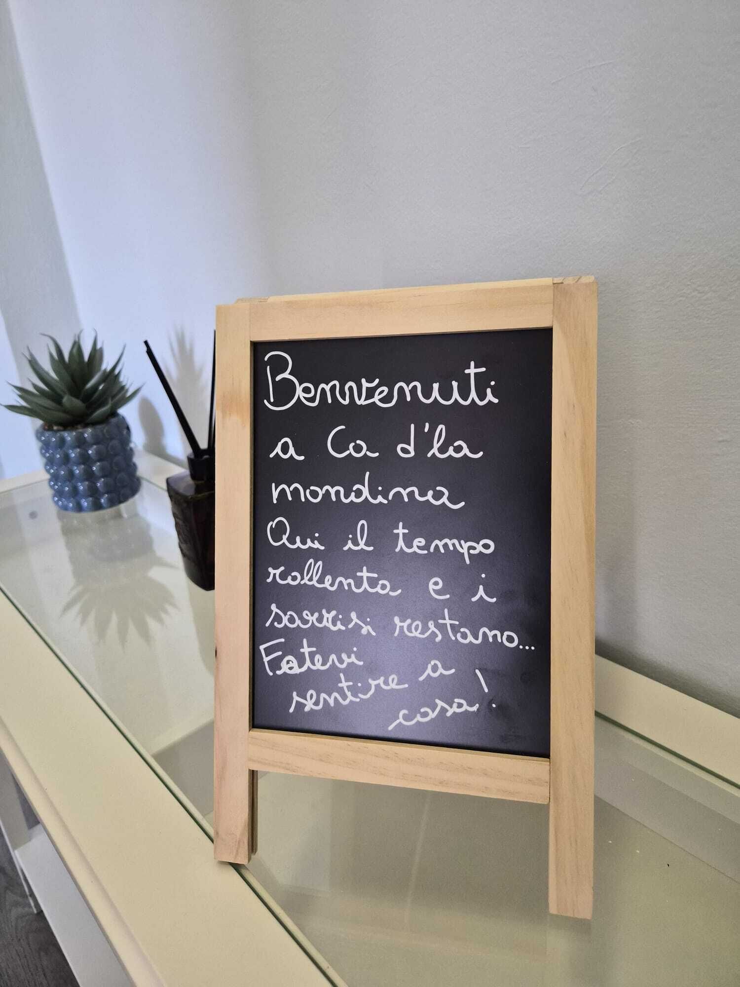 Un tableau noir sur lequel est écrit un message en italien, posé sur un support en bois.