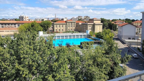 Piscina rodeada por árvores, com edifícios ao fundo.
