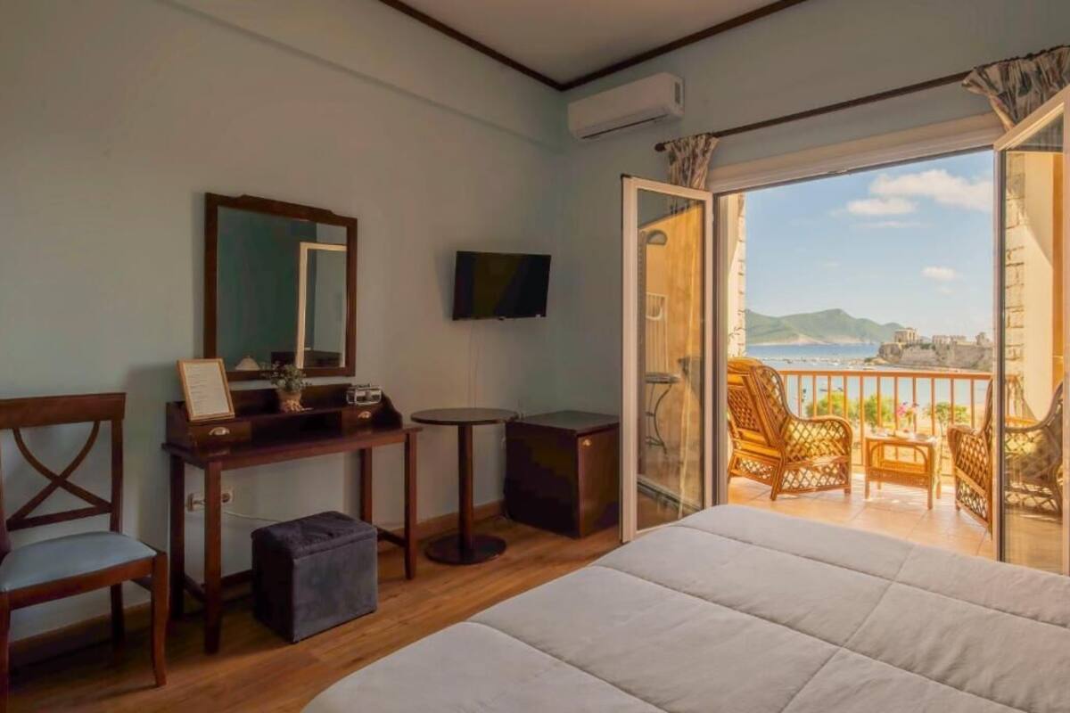 A bedroom with a bed, a desk with a chair, a television, and a balcony with outdoor furniture.