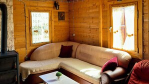 A cozy cabin interior with a wooden ceiling, a sofa, a chair, a table, and a fireplace. - Cabin Varde | 2-bedroom cabin in charming Žabljak (Žabljak)