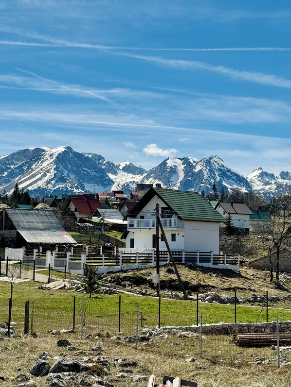 A rural village with houses, a fenced area, and snow-capped mountains in the background.