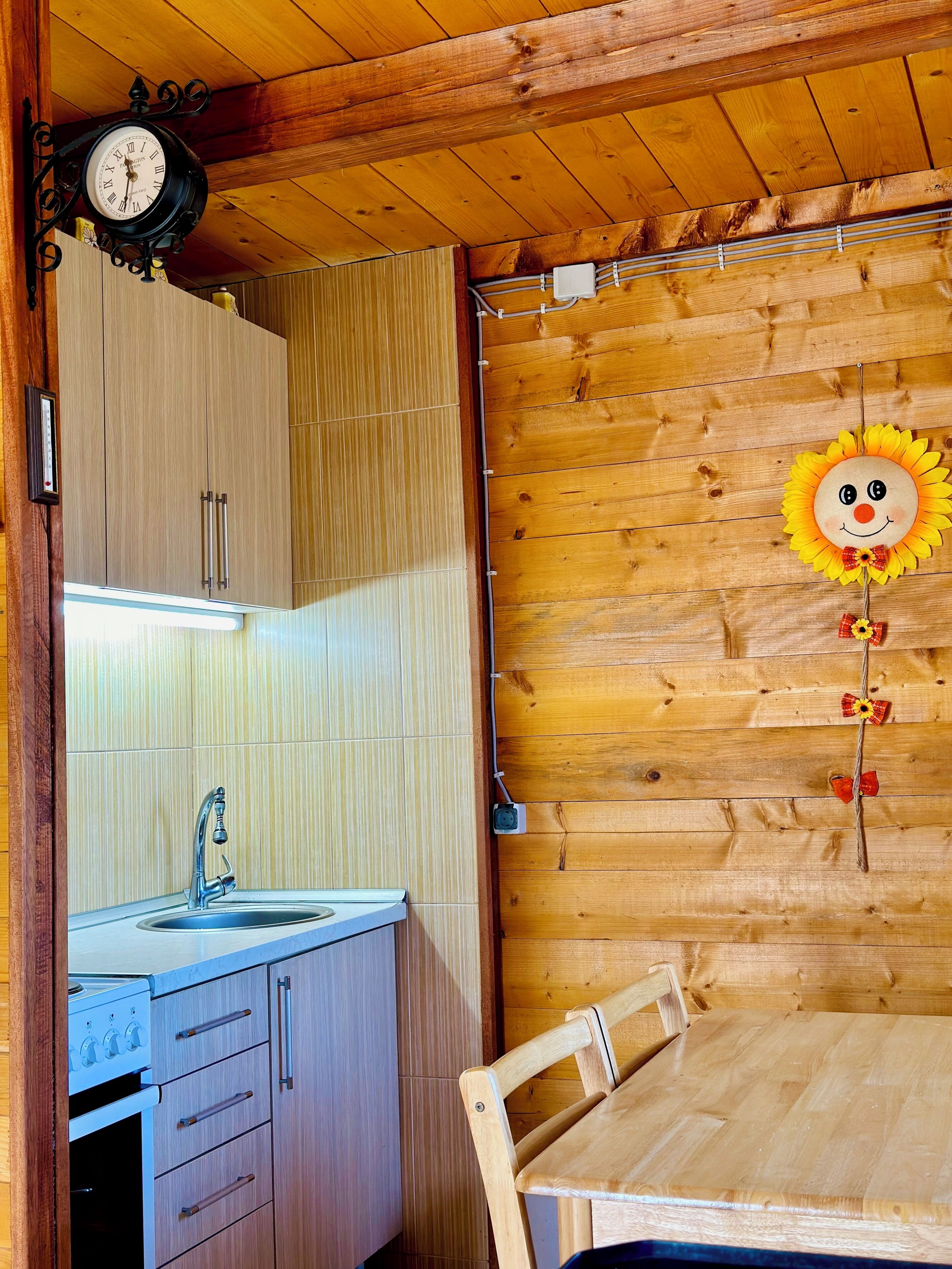 A wooden interior with a wooden table, a sink, cabinets, a clock, and a wall decoration.