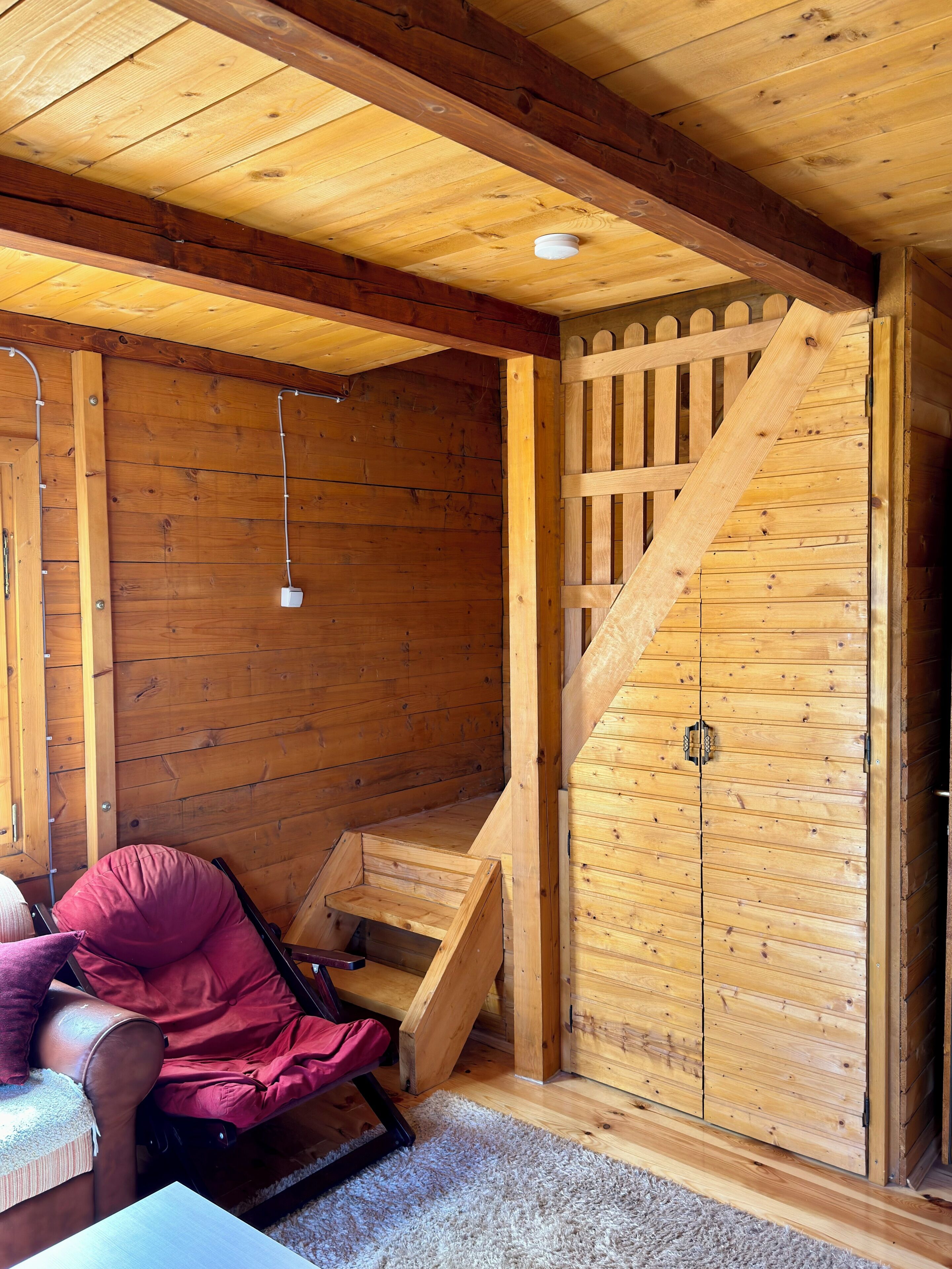 Ein Holzinnenraum mit einer Treppe, einem gepolsterten Sessel und einer Tür mit Holzgitter.