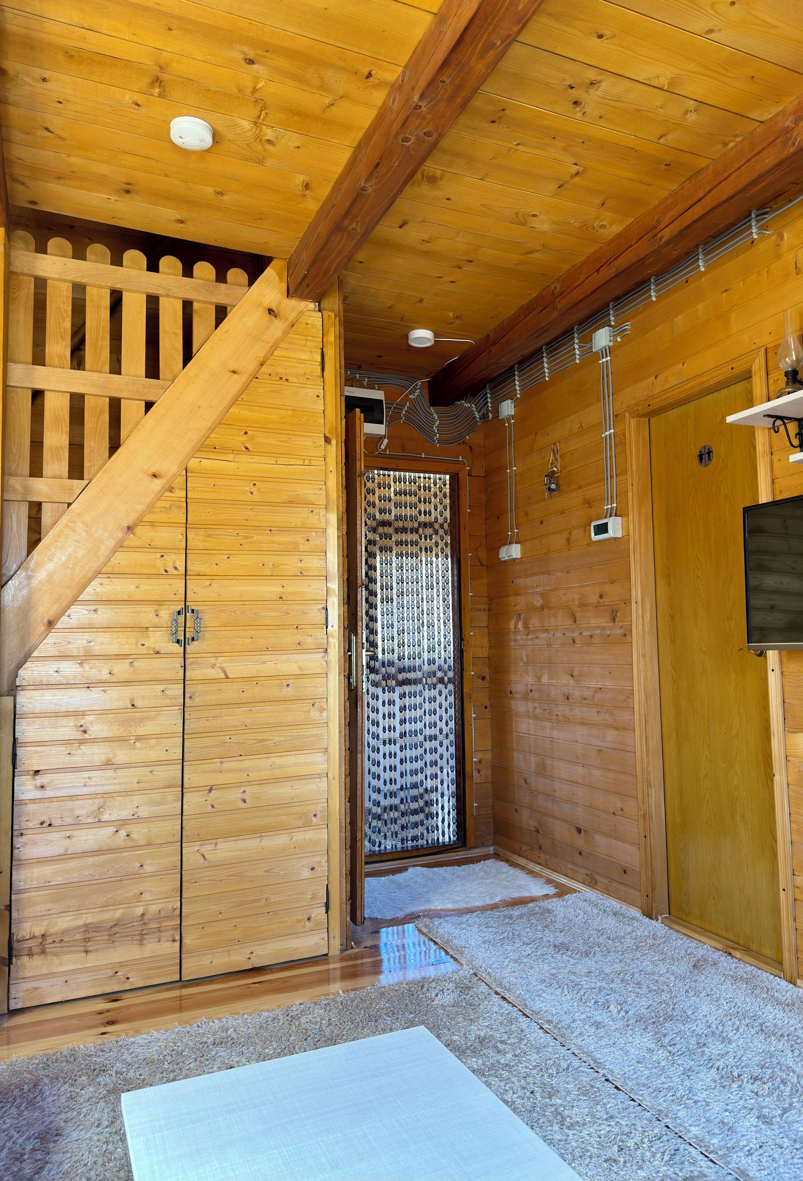 A wooden interior with a staircase, a door with a metal gate, and a wall-mounted light fixture.