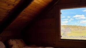A bedroom with a sloped ceiling, a window with a view of a rural landscape, and patterned bedding. - Cabin Varde | 2-bedroom cabin in charming Žabljak (Žabljak)