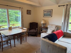 A cozy living room with a dining table, two armchairs, a sofa, and a lamp. - Cozy 1-bedroom cabin in quaint Coplin, with AC and gas fireplace. (Coplin plantation)