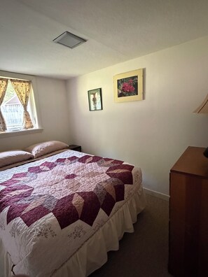 A bedroom with a bed, a window with curtains, a wall-mounted picture frame, and a bedside table. - Cozy 1-bedroom cabin in quaint Coplin, with AC and gas fireplace. (Coplin plantation)