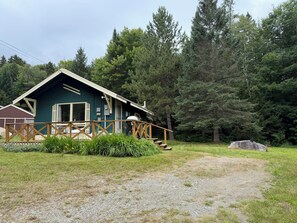 A cabin with a deck, surrounded by forest. - Cozy 1-bedroom cabin in quaint Coplin, with AC and gas fireplace. (Coplin plantation)