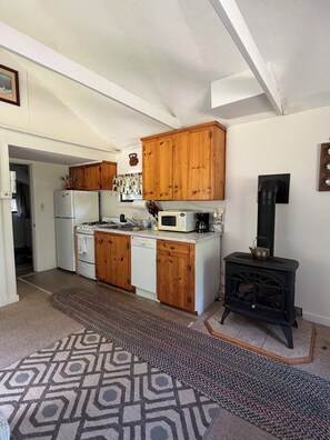A compact kitchen with wooden cabinets, a gas stove, a microwave, and a black wood-burning stove. - Cozy 1-bedroom cabin in quaint Coplin, with AC and gas fireplace. (Coplin plantation)