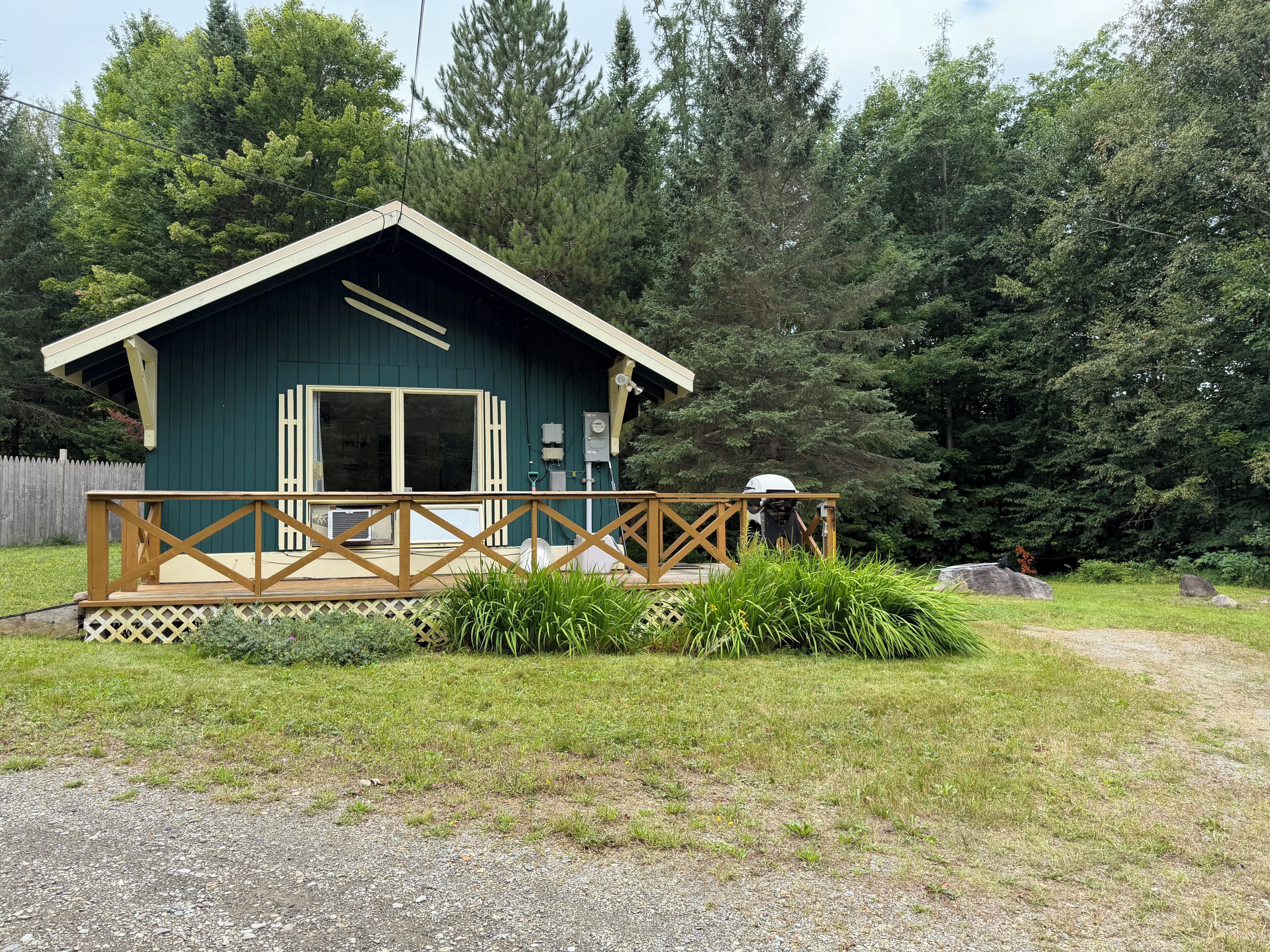 Une petite cabane dotée d’un porche et d’une terrasse, entourée d’une forêt dense.