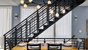 A dining area with a staircase, wooden table, chairs, and a chandelier. - Obermiller House ~ Spectacular Sunset~Modern~Rooftop~AC+Games+Parking (Seattle)