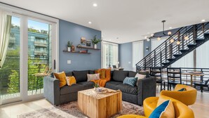 A modern living room with a sofa set, a coffee table, and a staircase. - Obermiller House ~ Spectacular Sunset~Modern~Rooftop~AC+Games+Parking (Seattle)