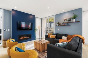 A modern living room with a fireplace, a flat-screen TV, and a sofa. - Obermiller House (Seattle)
