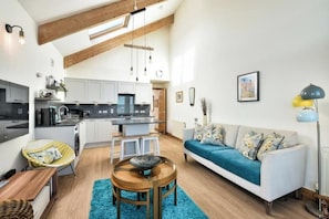 Eine moderne Küche mit weißen Schränken, ein Essbereich mit einem blauen Teppich und ein Wohnzimmer mit einer Couch und einer Lampe.