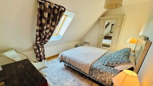Une chambre à coucher comprenant un lit, un bureau, une chaise, une lampe, une fenêtre avec des rideaux et un miroir.