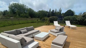Une terrasse en bois aménagée avec du mobilier d’extérieur, notamment des canapés et des fauteuils de relaxation.