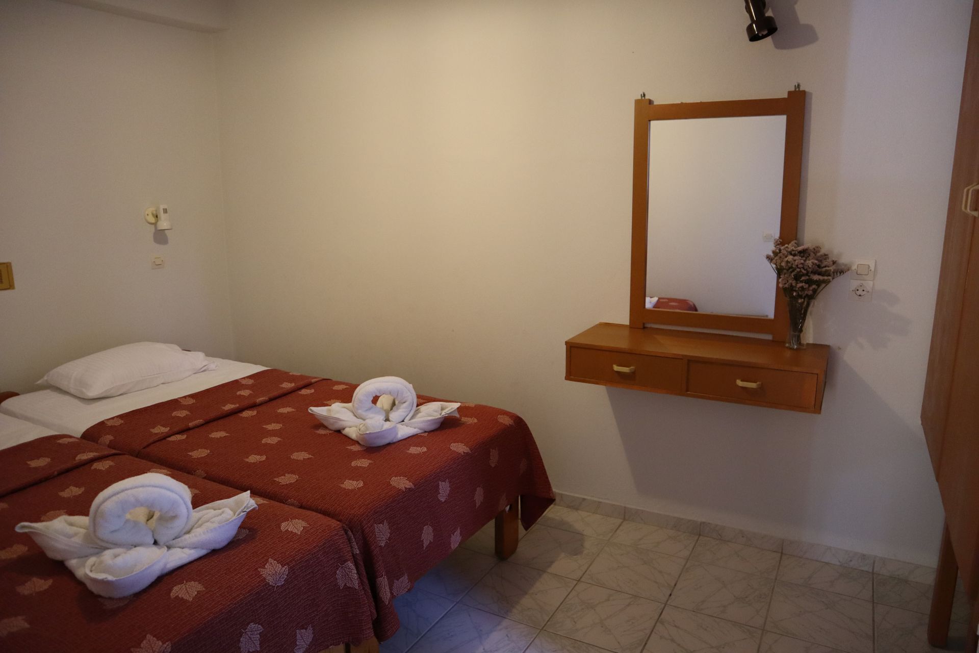 Une chambre d’hôtel avec deux lits, une commode en bois avec un miroir et un vase rempli de fleurs.
