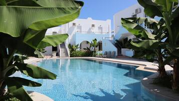 Un'area piscina con una piscina azzurra e cristallina, edifici bianchi e rigogliosa vegetazione.