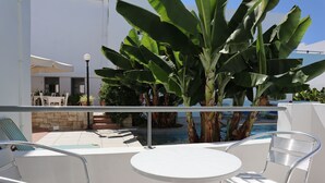 Ein Balkon mit Pool, weißen Metallstühlen und großen Bananenpflanzen.