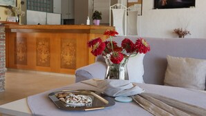Ein Empfangsbereich mit Holztresen, einer Vase mit roten Blumen, einer Couch und einem an der Wand befestigten Fernseher.