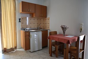Una cocina compacta con armarios de madera, lavavajillas integrado, salpicadero de azulejos y una zona de comedor con mesa y sillas.