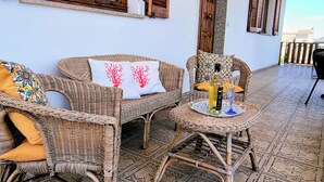 Móveis de vime, um tapete estampado e uma mesa com uma garrafa e um copo.