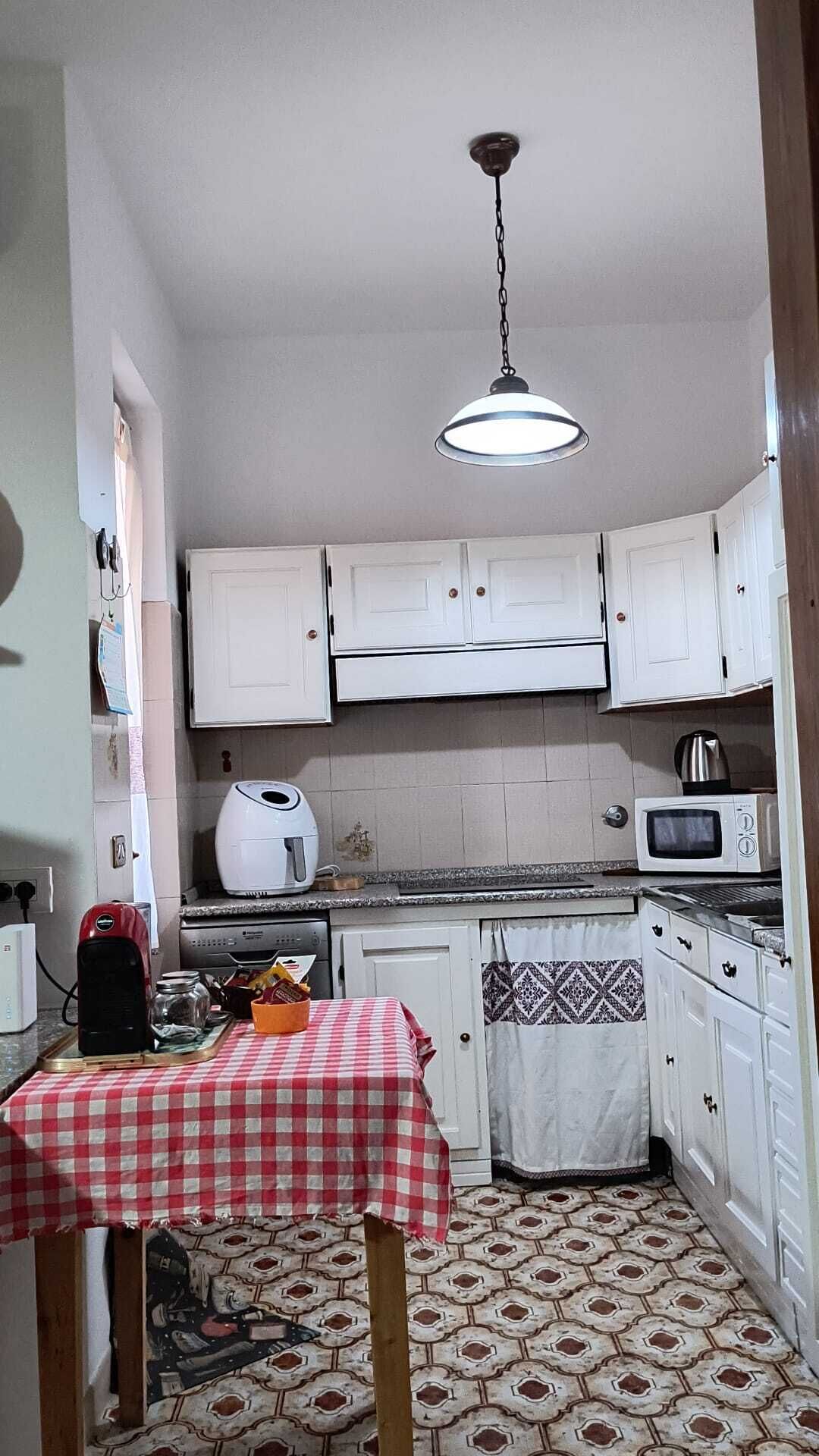A compact kitchen with white cabinets, a microwave, a coffee maker, and a table with a checkered tablecloth.