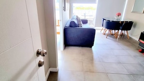 Un salon moderne avec un canapé, une table à manger et des chaises, et une vue sur une terrasse extérieure, accessible par une porte vitrée.
