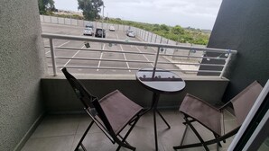 Un balcon avec deux chaises et une petite table, donnant sur un parking où sont garées plusieurs voitures.