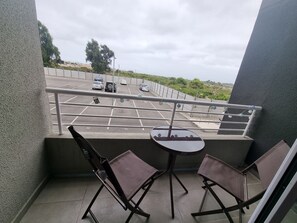 Ein Balkon mit zwei Stühlen und einem kleinen Tisch, mit Blick auf einen Parkplatz mit mehreren Autos.