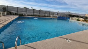 Une piscine rectangulaire à l’eau d’un bleu limpide, entourée d’une terrasse en béton et d’une clôture en métal blanc.