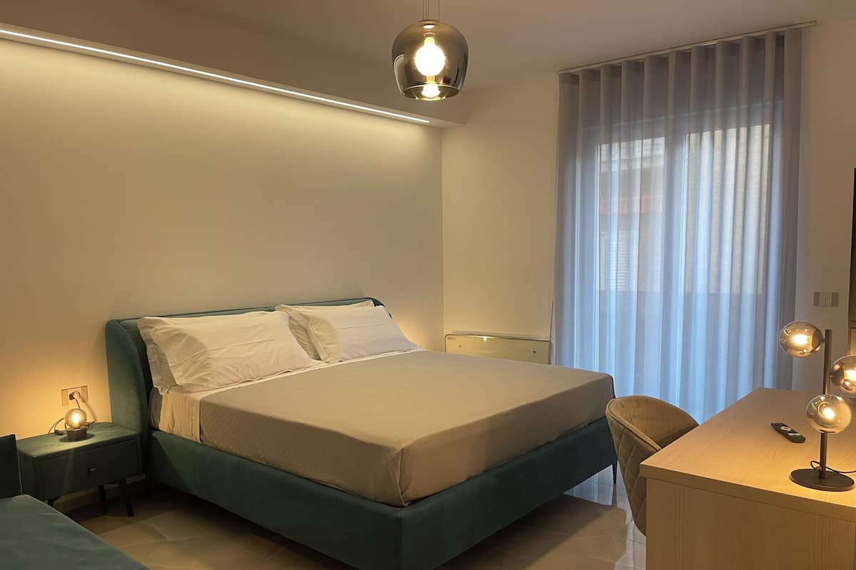 Un dormitorio moderno con cama, mesita de noche, lámpara y un escritorio con silla.